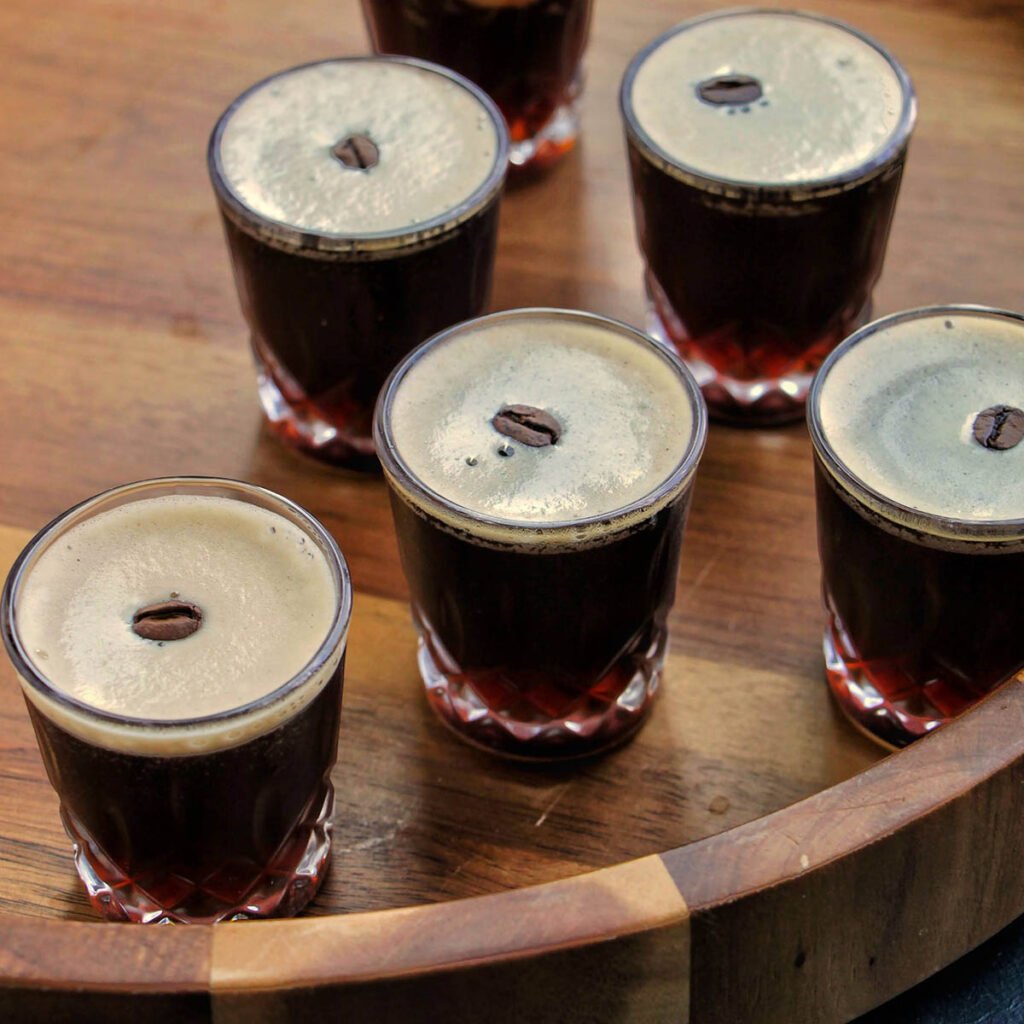 6 New Year's Eve Shots Espresso martini shots with coffee bean garnish on a wooden tray
