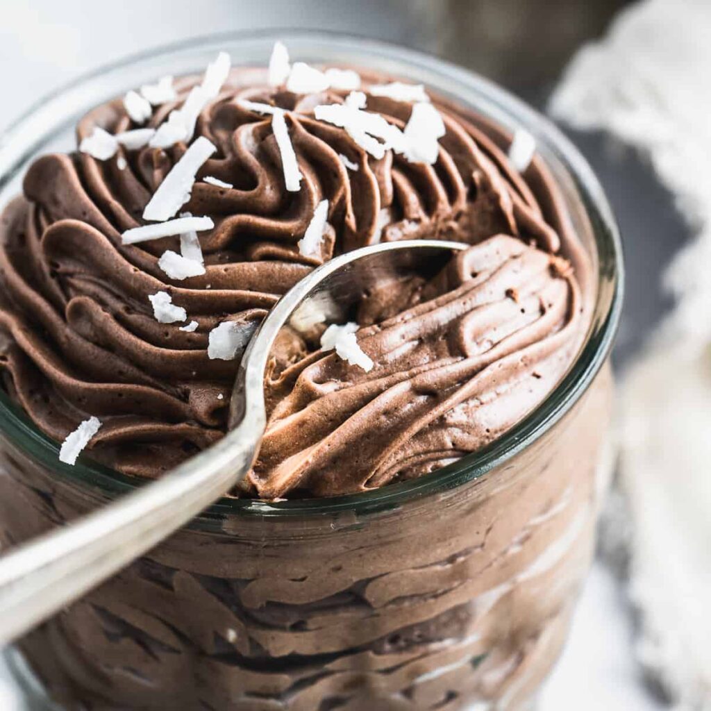 Rich chocolate mousse dessert in a glass jar, topped with coconut flakes.