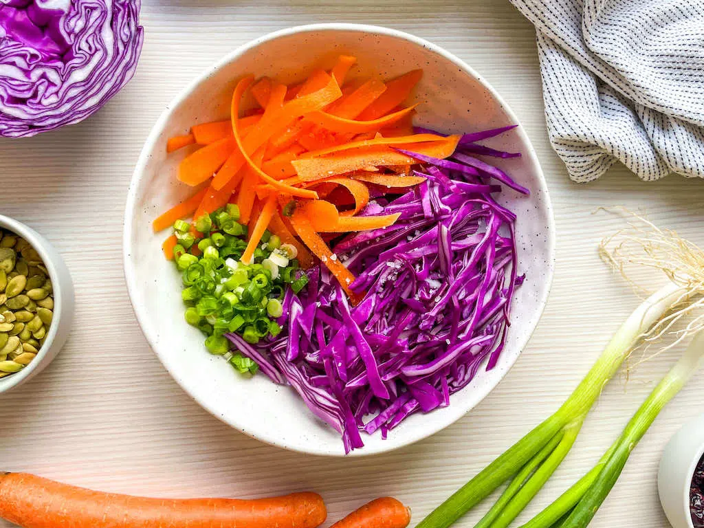 Thinly sliced carrots, red cabbage and green onions in a stoneware bowl for carrot and red cabbage salad with lemon tahini dressing.