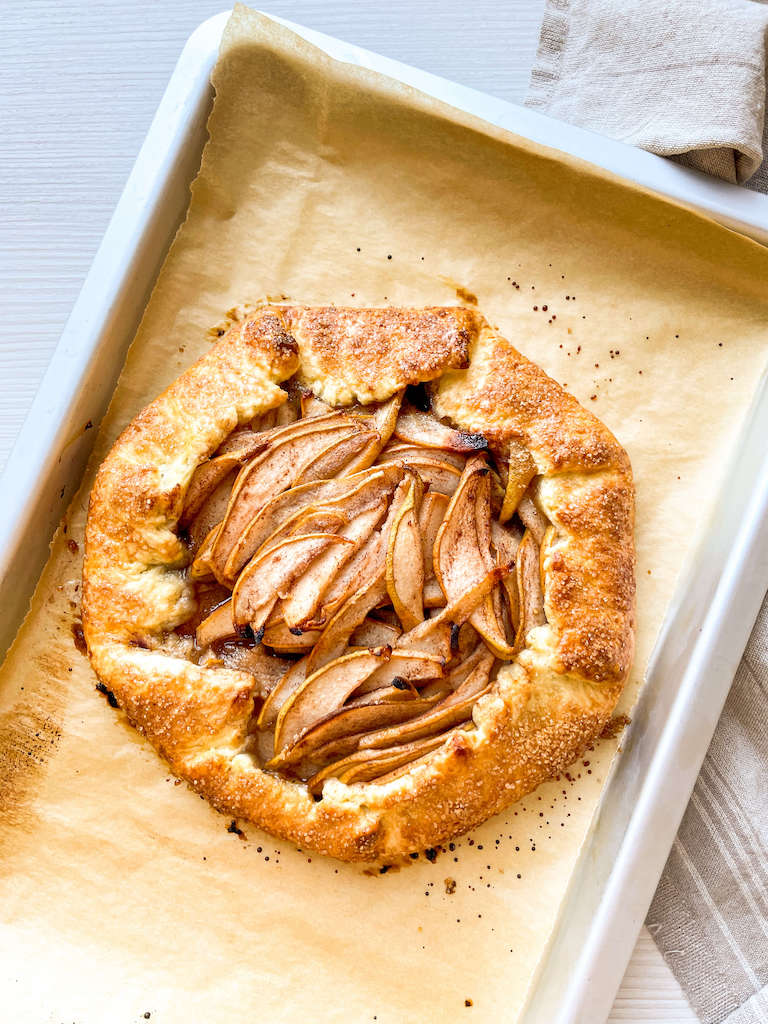 A baked rustic pear galette on a parchment paper lined baking sheet.