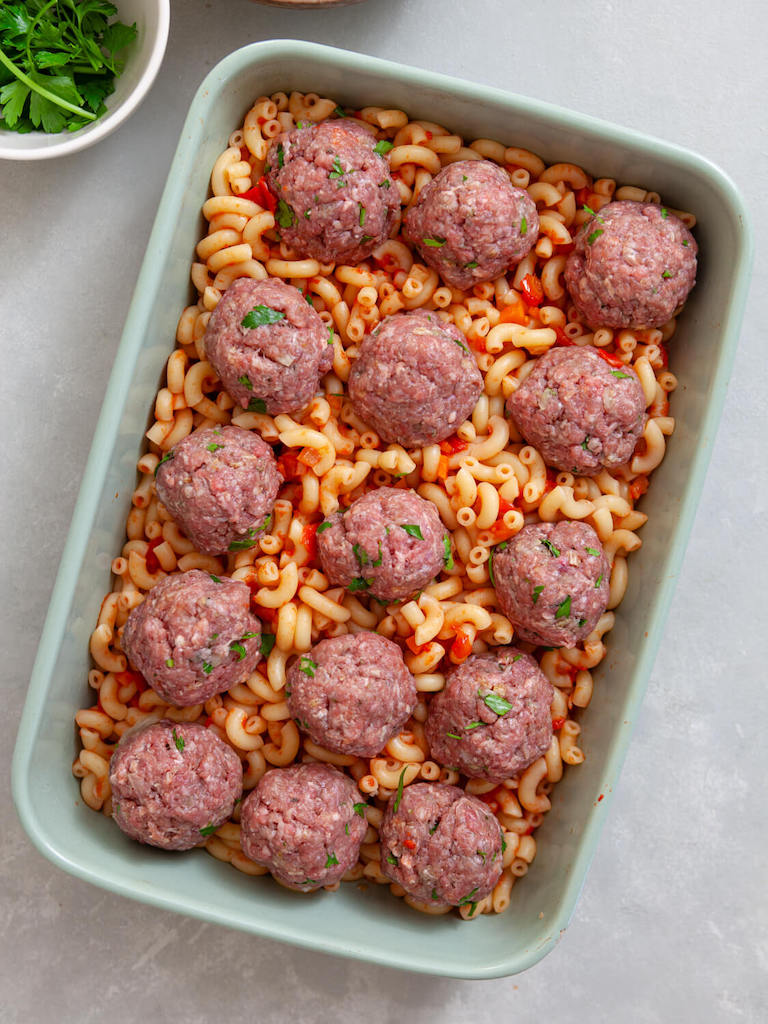 Meatballs on top of the pasta layer in a casserole dish.