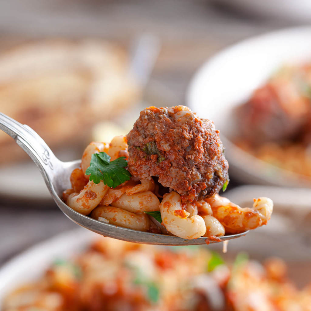 A spoonful of meatball casserrole with a meatball and noodles.