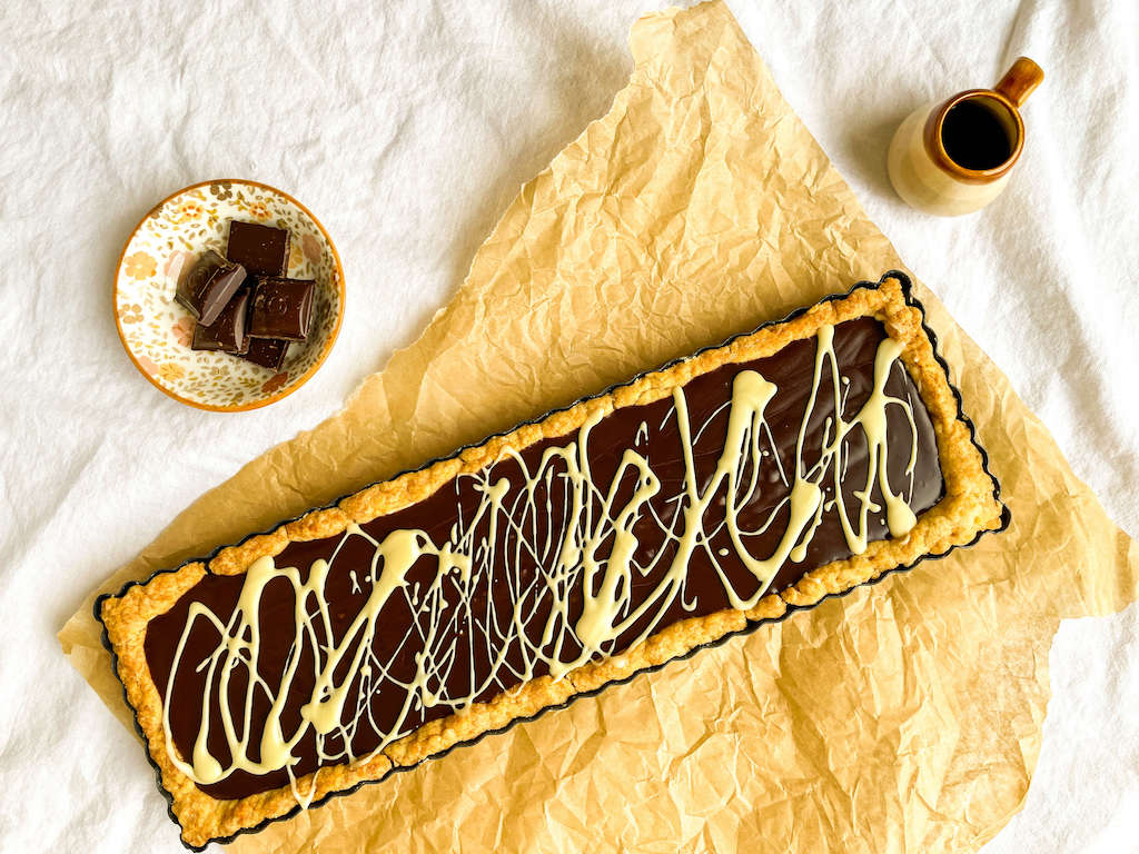A decadent chocolate kahlua tart on a piece of parchment paper with a bowl of chocolate chunks.