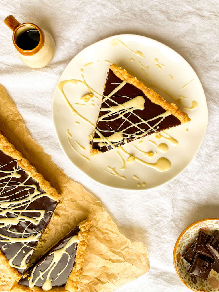 A slice of Kahlua chocolate tart on a serving plate drizzled with white chocolate and flakey sea salt.