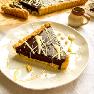 An individual serving of chocolate kahlua tart on a serving plate drizzled with white chocolate.