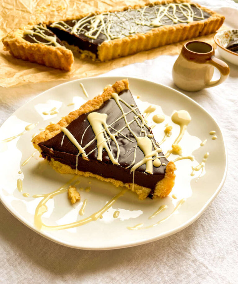 An individual serving of chocolate kahlua tart on a serving plate drizzled with white chocolate.