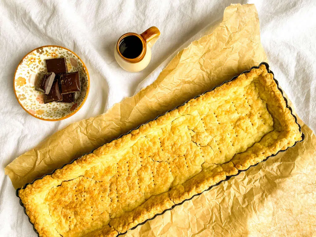 A fully baked tart crust in a tart shell on a piece of parchment paper.