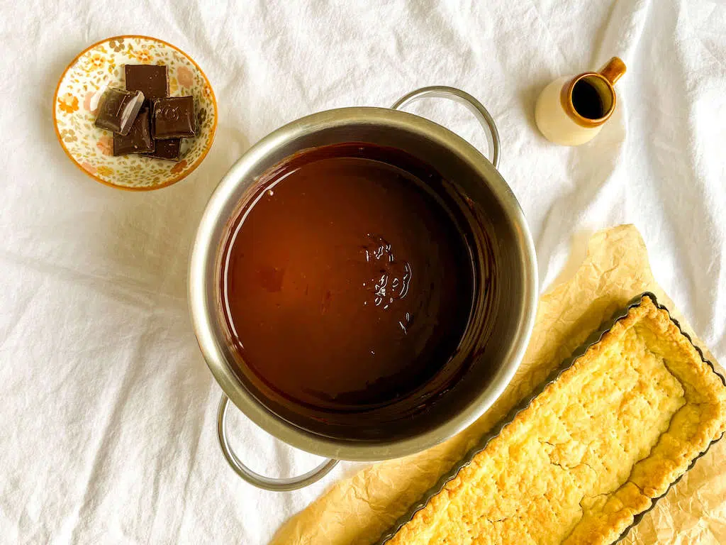 The melted chocolate and havy cream in a sauce pan next to the cooled tart shell.