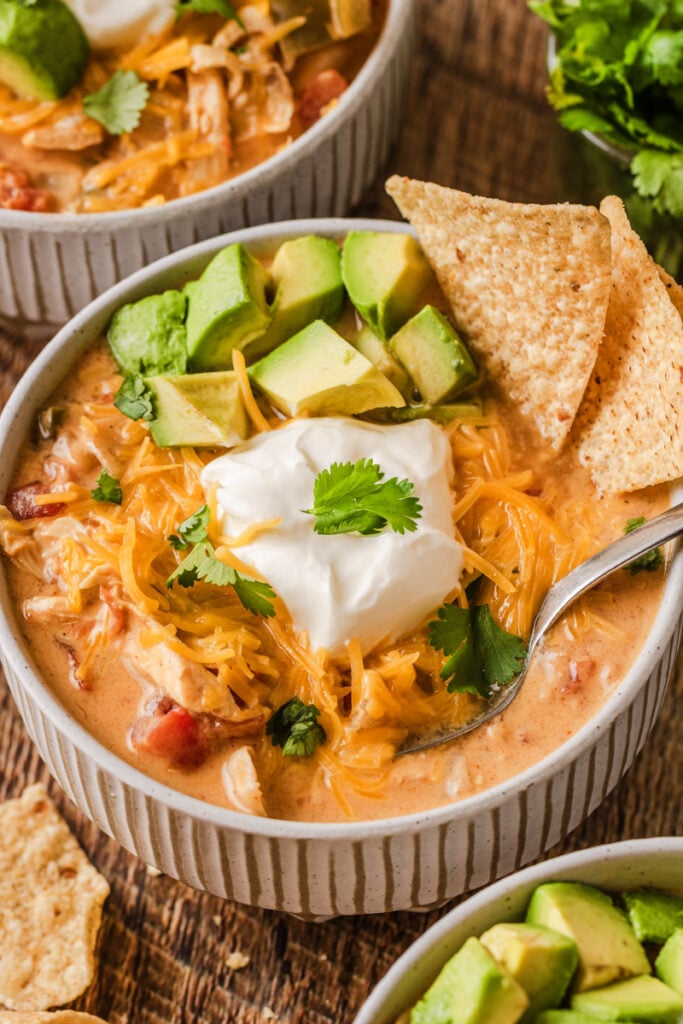 Creamy chicken tortilla soup with avocado, shredded cheddar, sour cream, cilantro, and chips