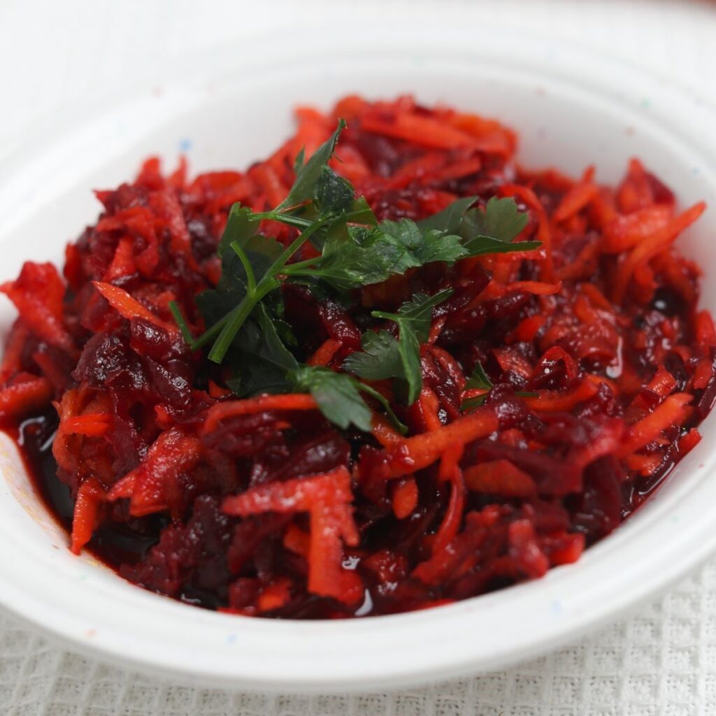Shredded beet and carrot salad with parsley in white bowl