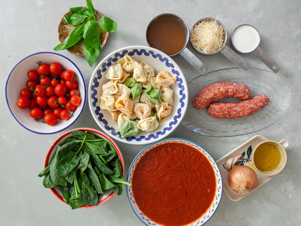 One skillet Italian Sausage and Tortellini ingredients including baby spinach, seasonings, Italian sausage, and cherry tomatoes.