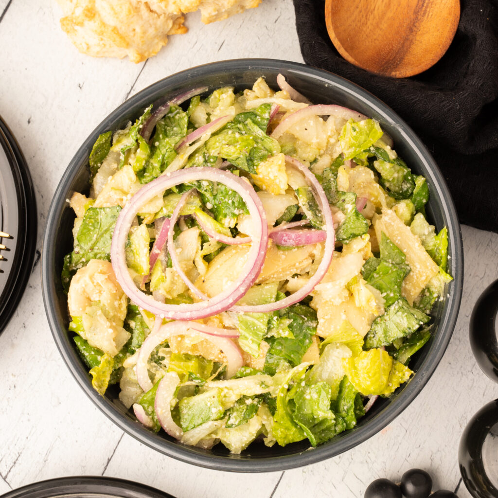 Fresh romaine salad with red onion rings, parmesan, and creamy dressing in bowl
