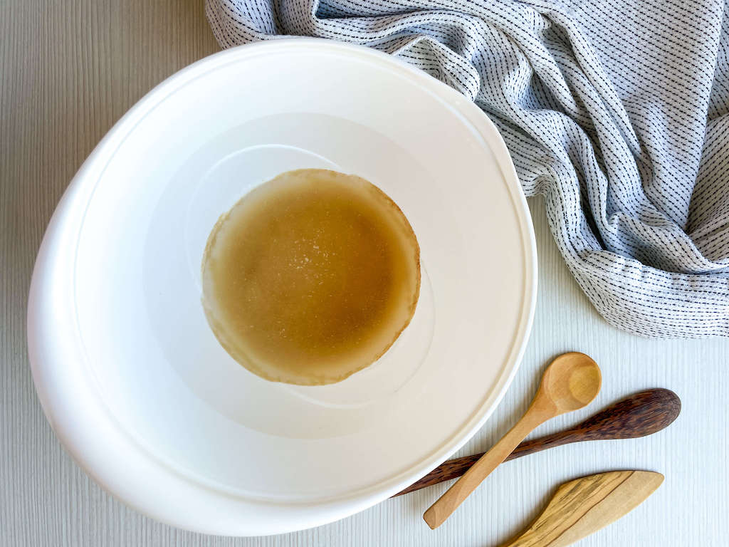 The active yeast, water, sugar, and salt in a white mixing bowl to make no knead pizza dough.