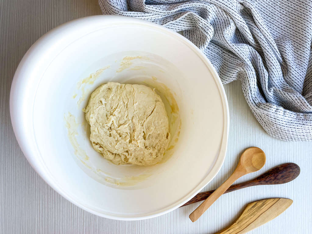 A stick ball of no knead pizza dough in a white mixing bowl.