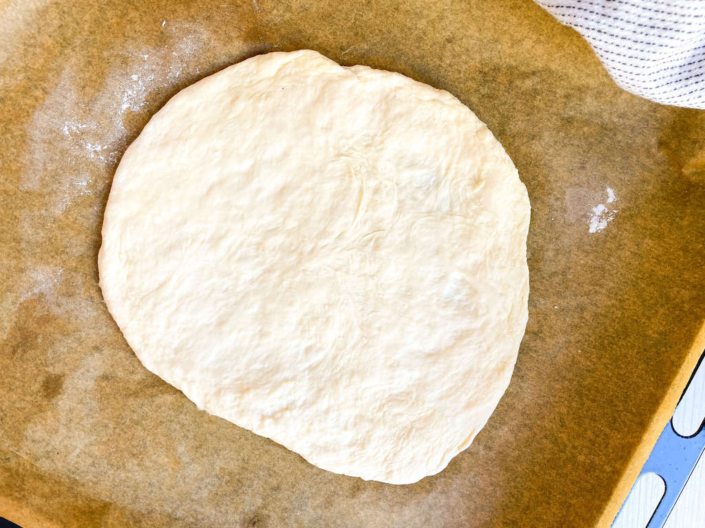 A rolled out piece of no knead pizza dough on a lightly oiled surface.