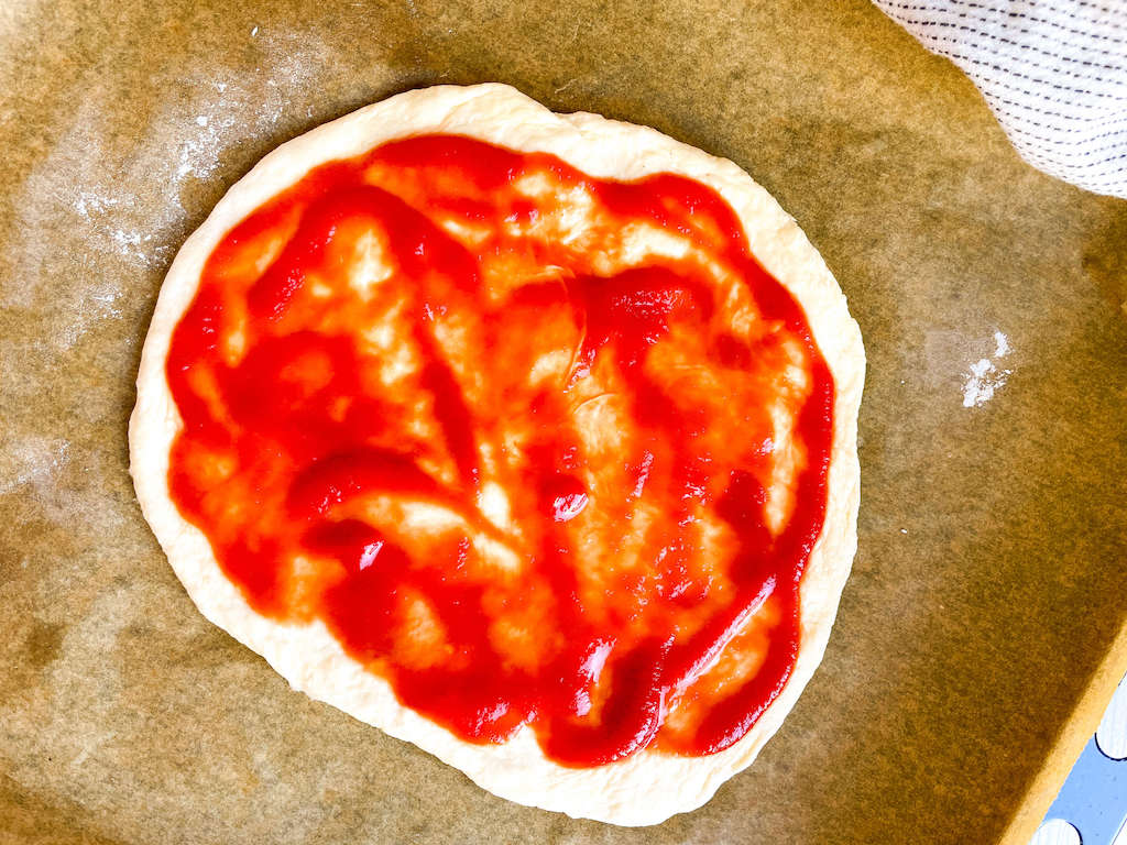 Pizza dough spread with marinara sauce for margherita pizza.