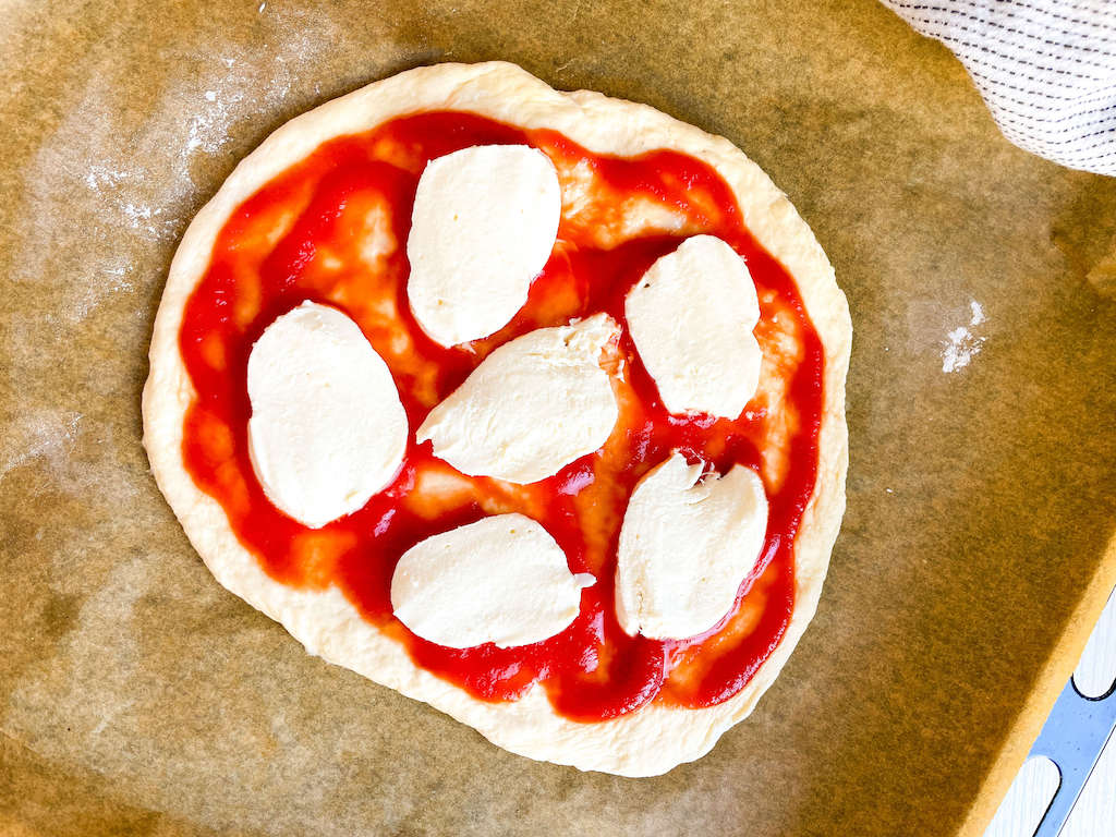 An unbaked margherita pizza topped with fresh mozzarella cheese.