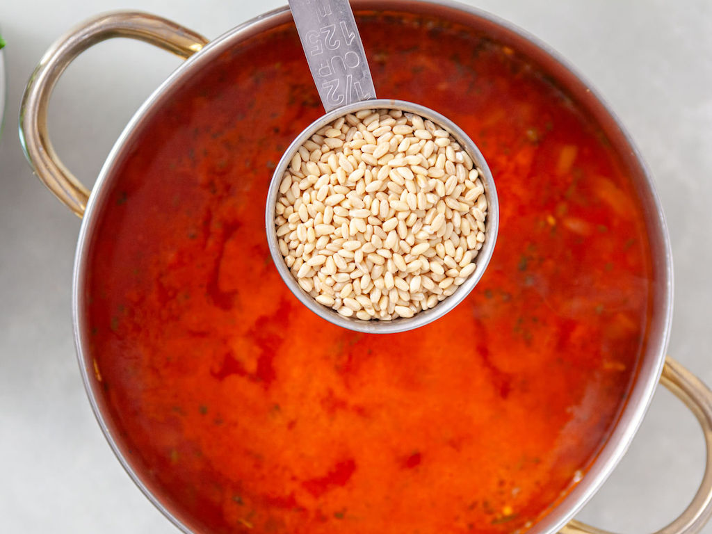 A measuring cup of pearl barley being added to the large soup pot.
