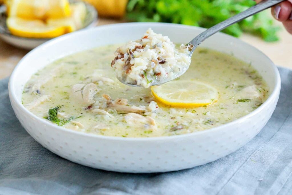 Creamy lemon chicken rice soup with dill in a bowl, spoon lifting a bite