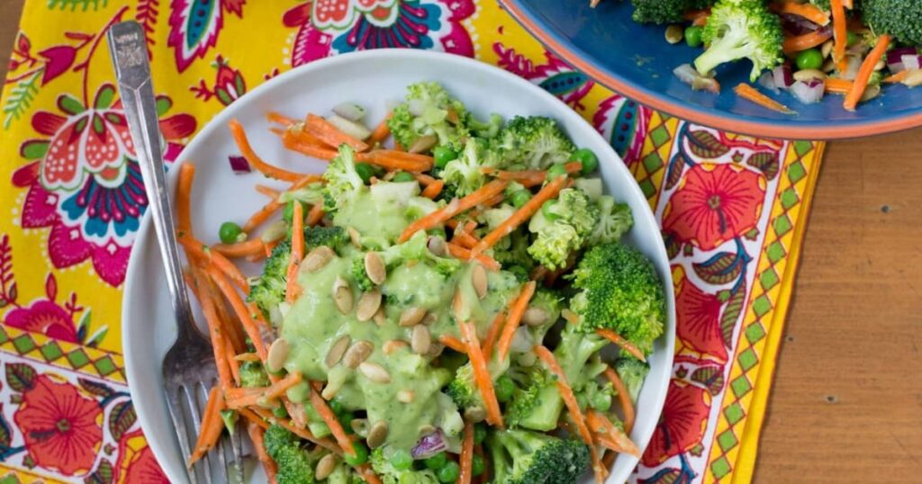 Vegan broccoli salad with carrots, peas, seeds and creamy avocado dressing