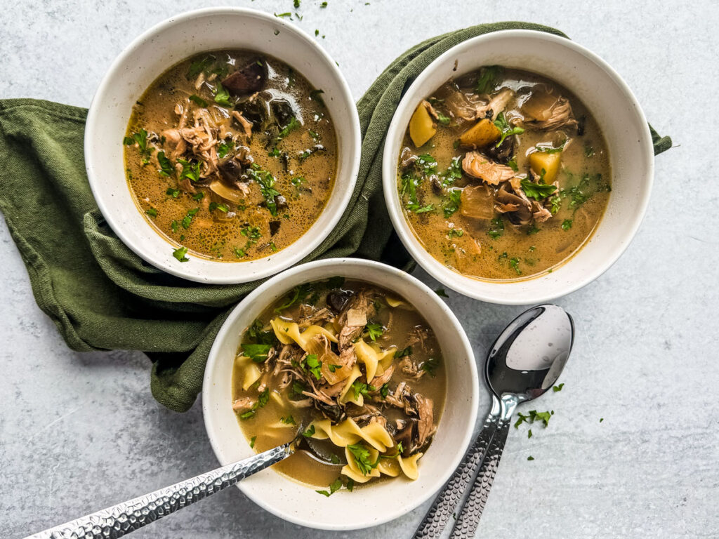 Overhead of three bowls of homemade chicken soup with mushrooms and noodles