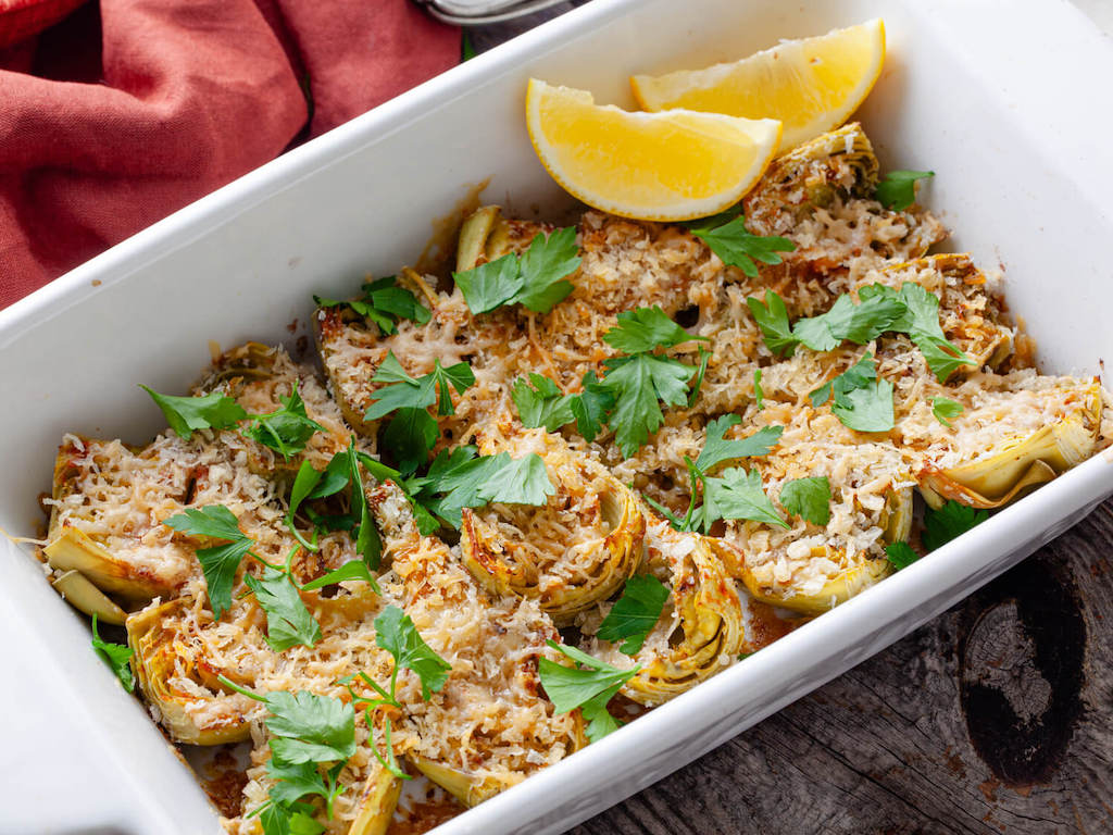Crispy artichoke hearts in a white casserole dish garnished with lemon slices and fresh parsley.
