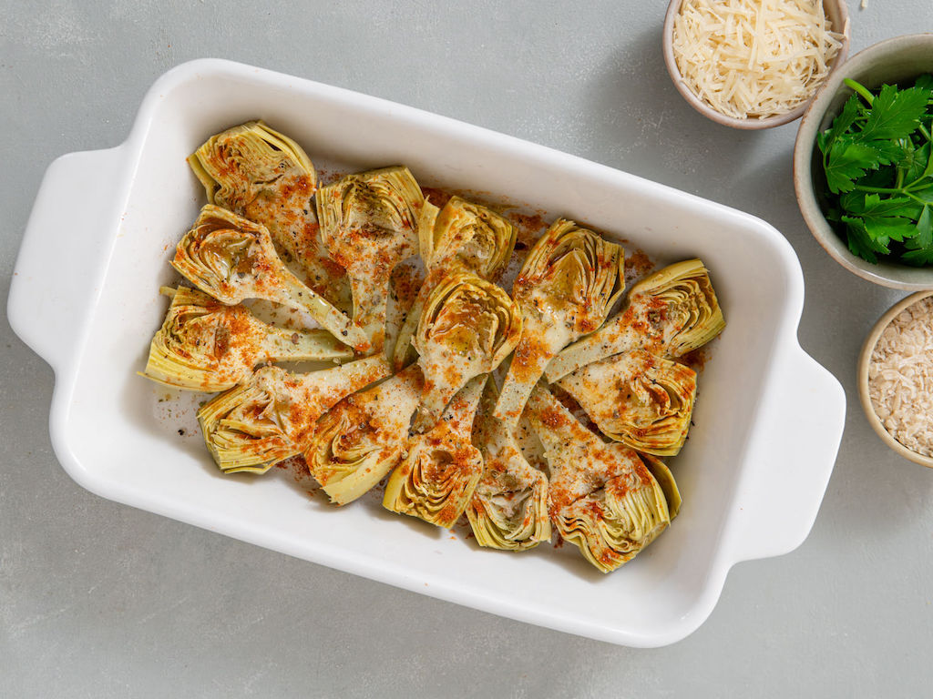 Artichoke hearts in a casserole dish tossed with paprika, thyme, and olive oil.