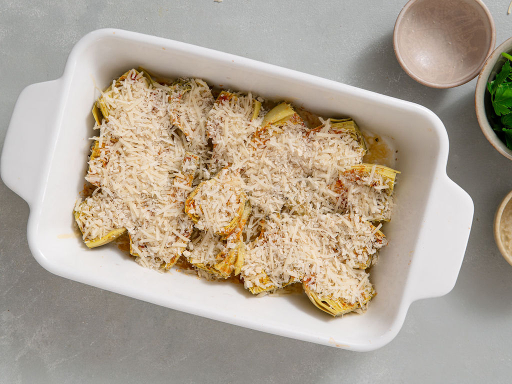 A casserole dish with the seasoned and baked artichoke hearts topped with breadcrumbs and parmesan cheese ready to bake again.