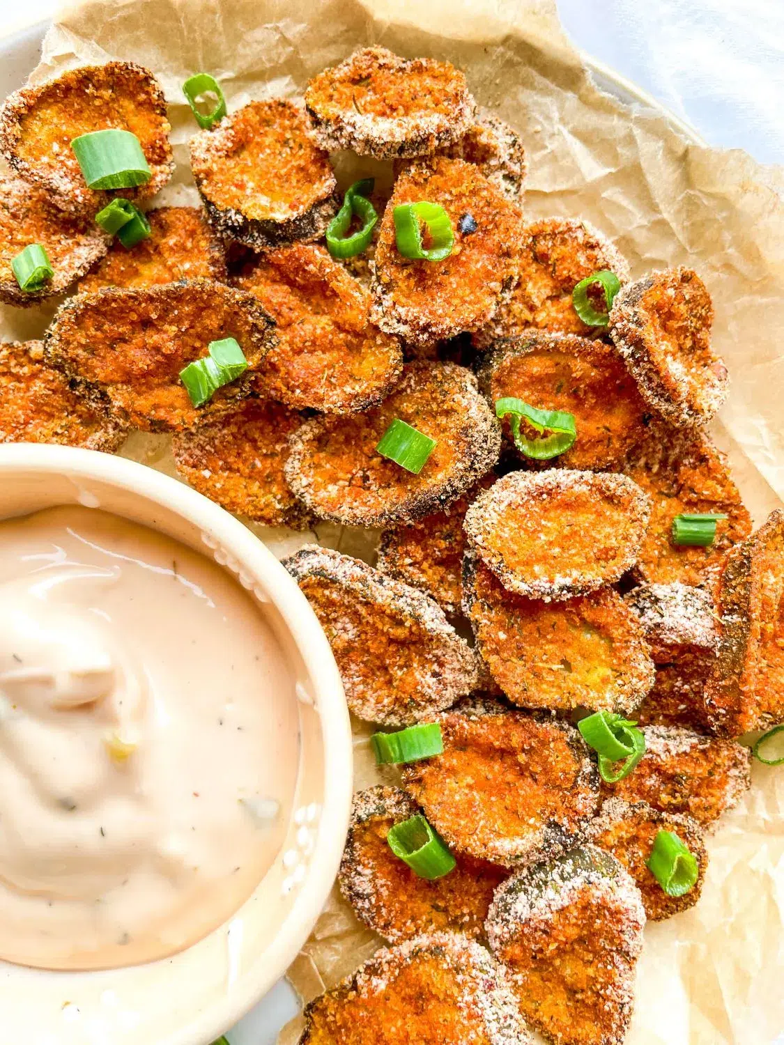 A plate of baked crispy pickle chips with sauce.