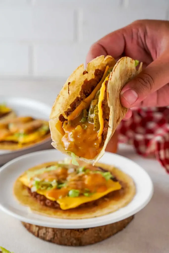 Cheesy beef taco with pickles and sauce held over plate