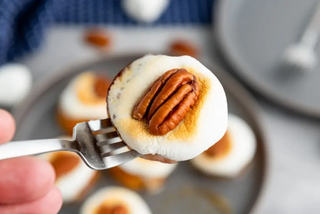 Close-up of a sweet potato snack idea with toasted marshmallow and pecan on top, served on a fork. Perfect small bite dessert for Thanksgiving or fall gatherings.