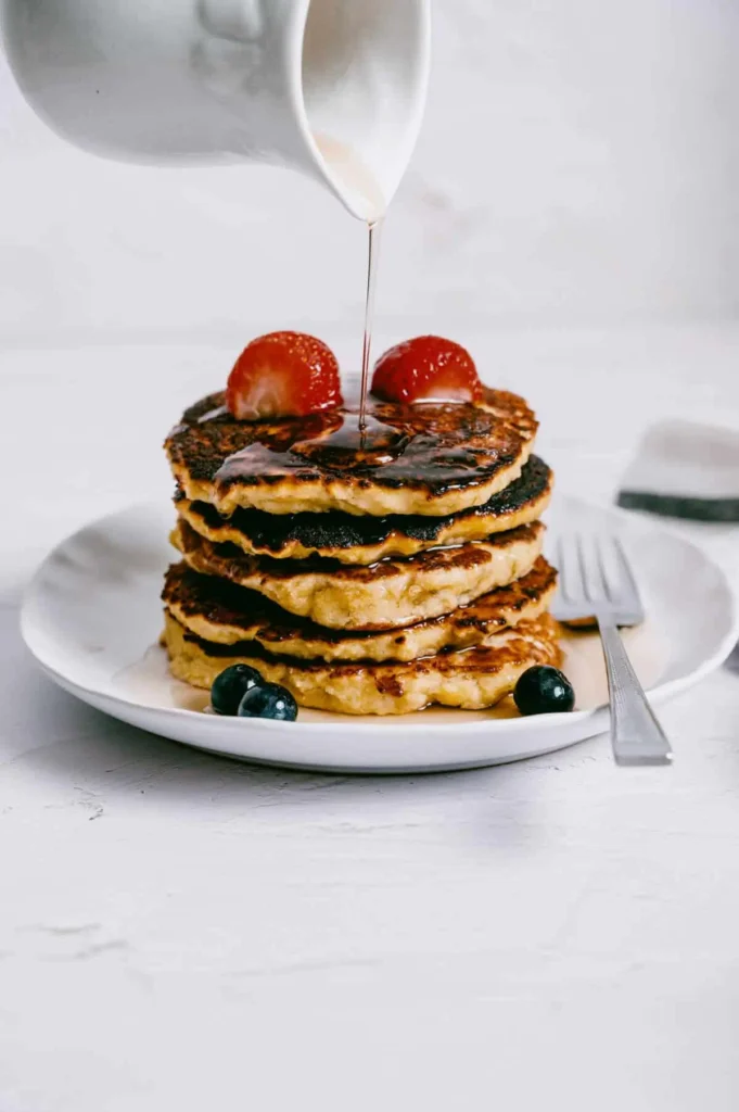 Golden almond flour pancakes topped with fresh strawberries and blueberries, drizzled with maple syrup. A perfect gluten-free and healthy breakfast choice