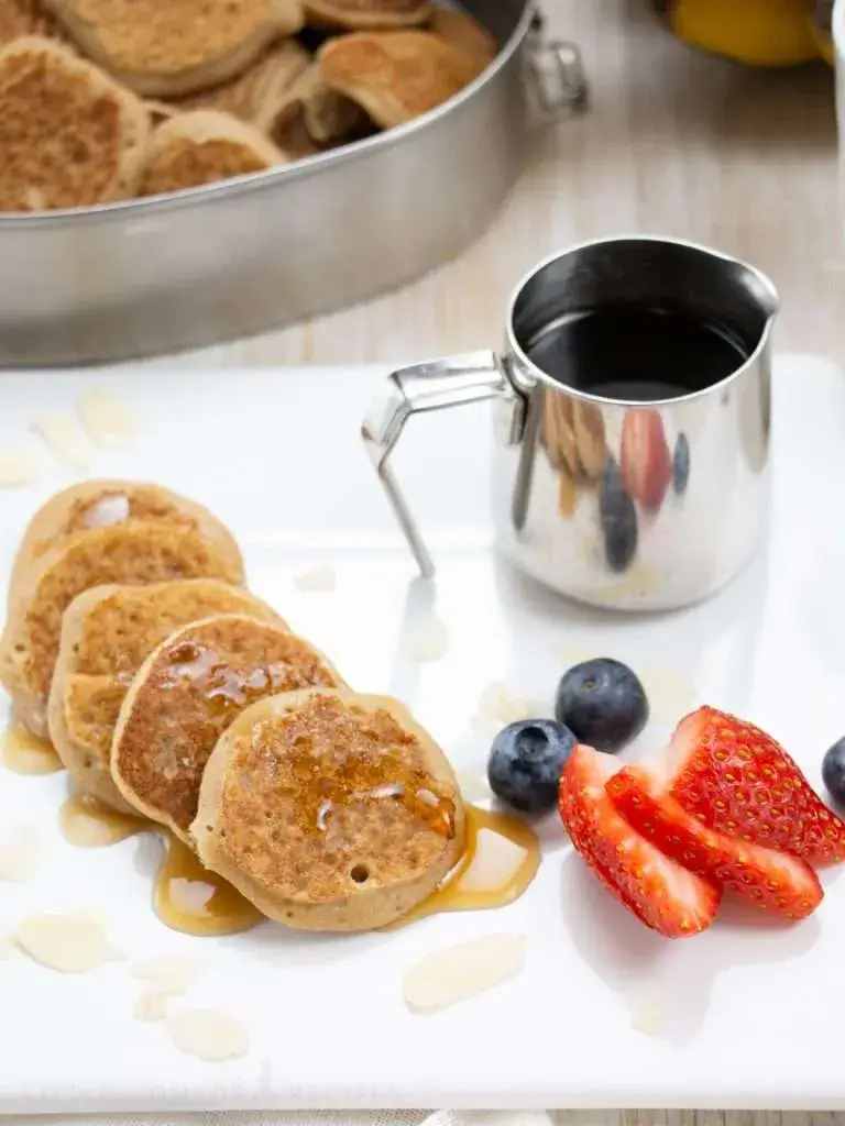 A stack of mini banana pancakes made with almond flour, served with syrup and fresh berries. A nutritious, gluten-free breakfast option loved by kids and adults.