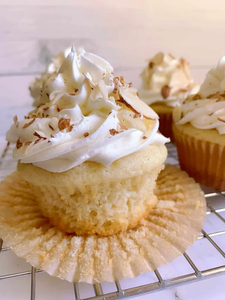  Soft and moist almond cupcakes topped with swirls of cream cheese frosting and garnished with sliced almonds, showcasing a delicate and indulgent dessert. 