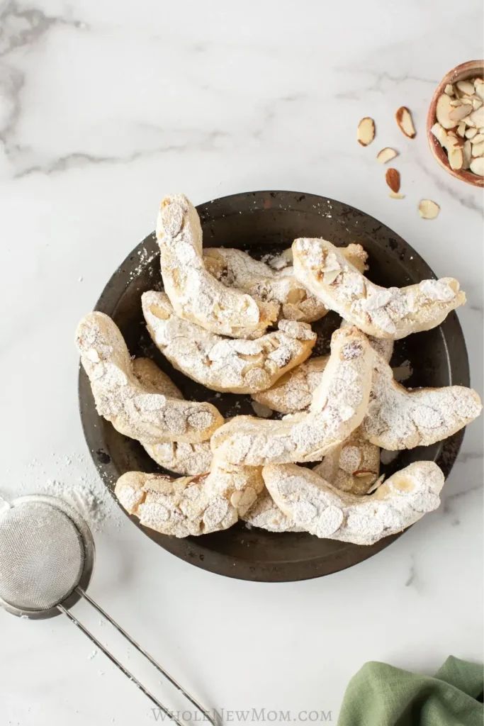 A plate of delicate almond crescent cookies dusted with powdered sugar, highlighting a crisp texture and festive presentation.