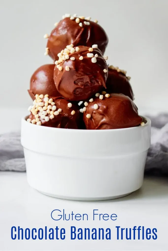   A bowl of rich chocolate banana truffles, coated in a glossy chocolate shell and sprinkled with crispy puffed quinoa for a gluten-free sweet treat.