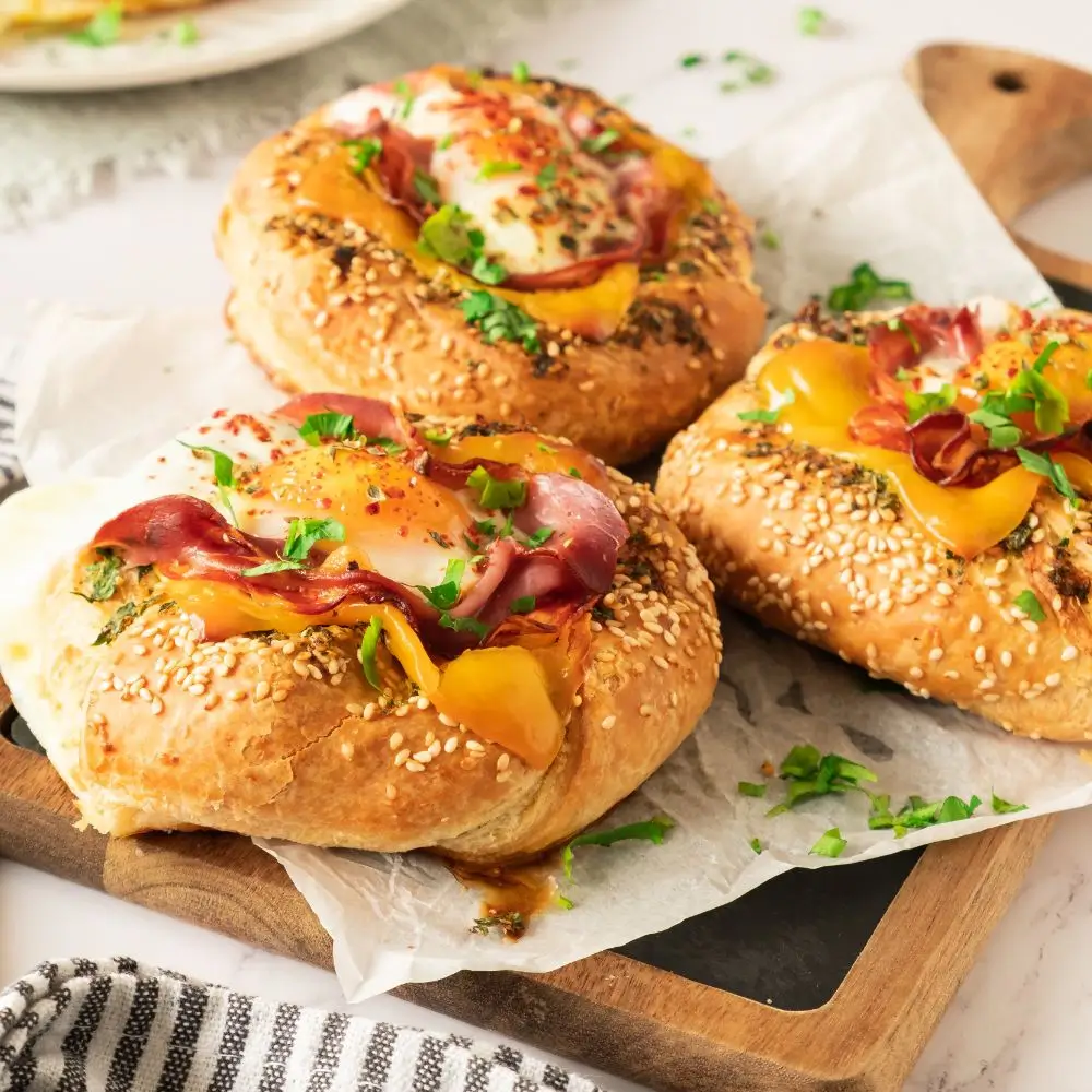 Bagel with egg and prosciutto topped with garlic butter on a wooden serving board, perfect for breakfast meal prep