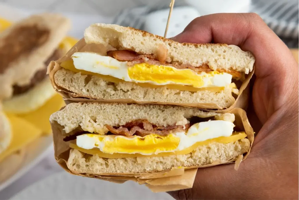 A hand holding a warm freezer breakfast sandwich, freshly reheated, with gooey cheese melting over a sausage patty – the ultimate make ahead breakfast.