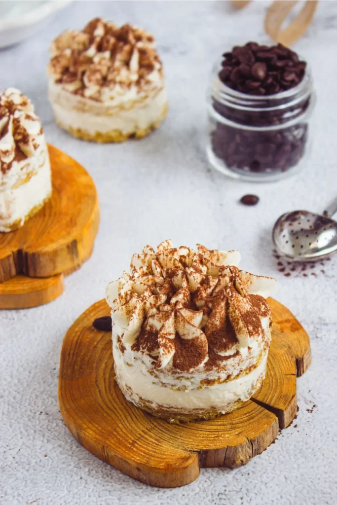 Mini tiramisu desserts arranged on wooden boards, with a jar of coffee beans and a spoon in the background.