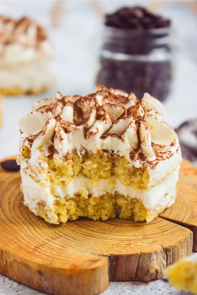 A close-up of a mini tiramisu with layers of coffee-soaked sponge and creamy mascarpone, topped with cocoa powder.