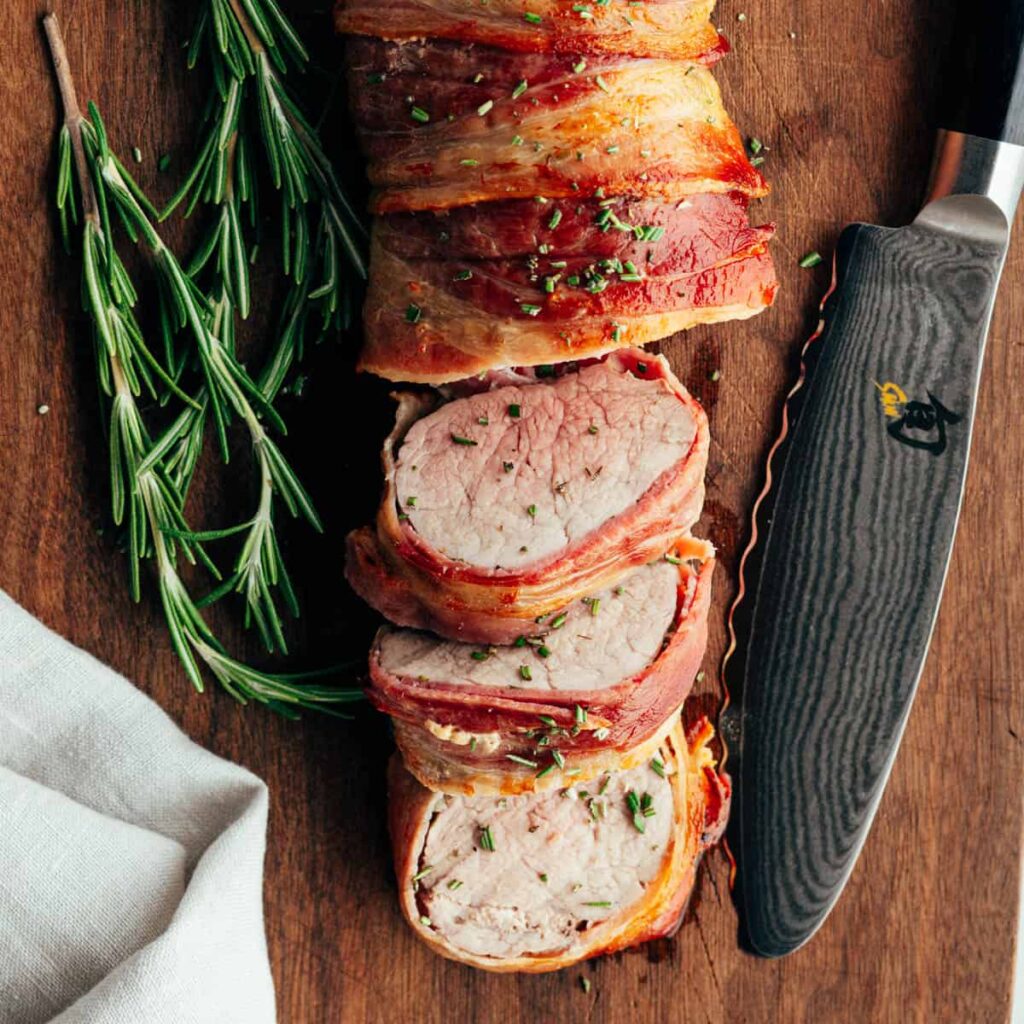 Bacon-wrapped pork tenderloin slices with rosemary and chef's knife