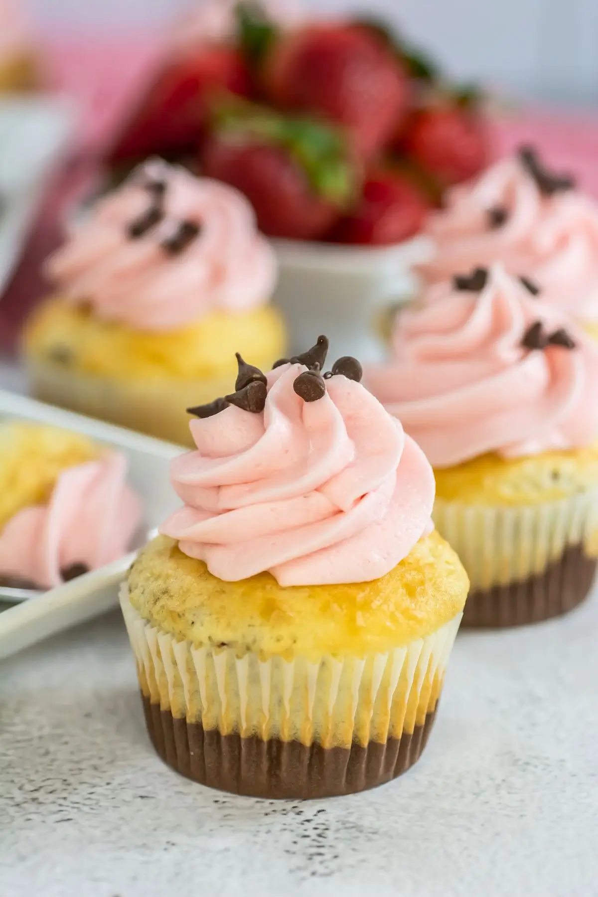 Close-up of Neapolitan cupcakes with cake mix topped with pink strawberry frosting and mini chocolate chips — an easy and fun cupcake recipe for kids.