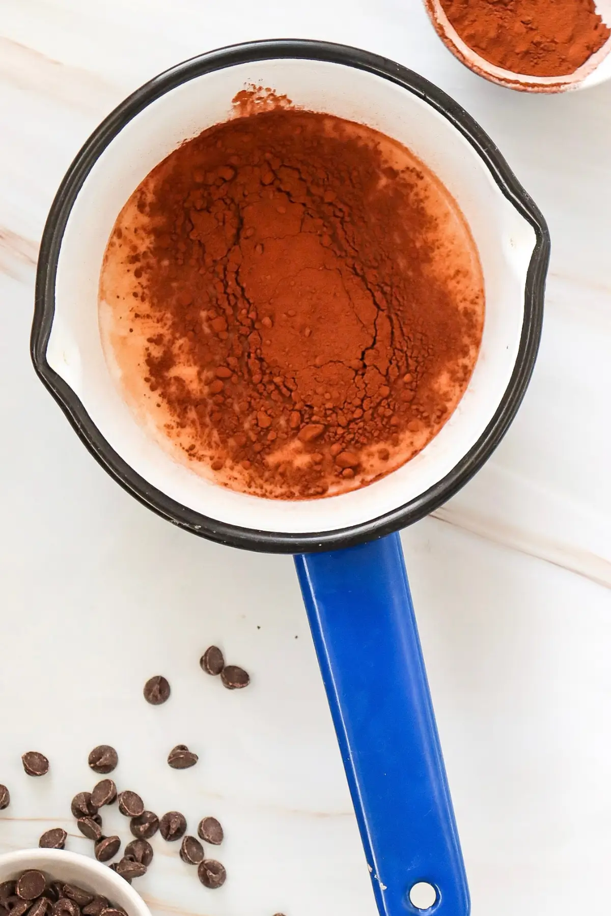 Sugar-free hot chocolate with almond milk in a pot, surrounded by chocolate chips.