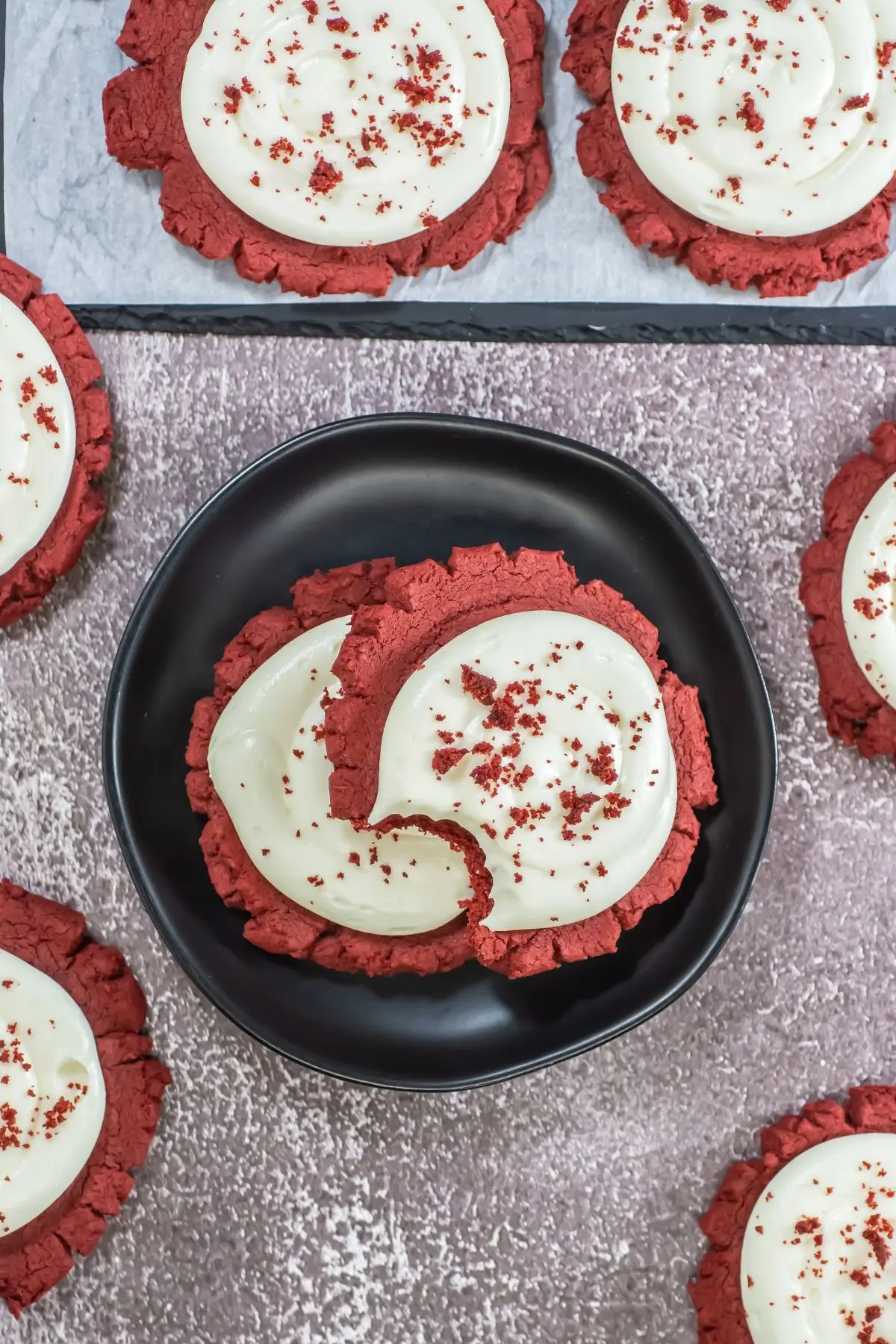 Red Velvet Crumbl Cookies (Crumbl Copycat) Close-up of copycat red velvet crumble cookies on a black plate with creamy frosting and red crumbs, awesome for holiday cookies or big gatherings.