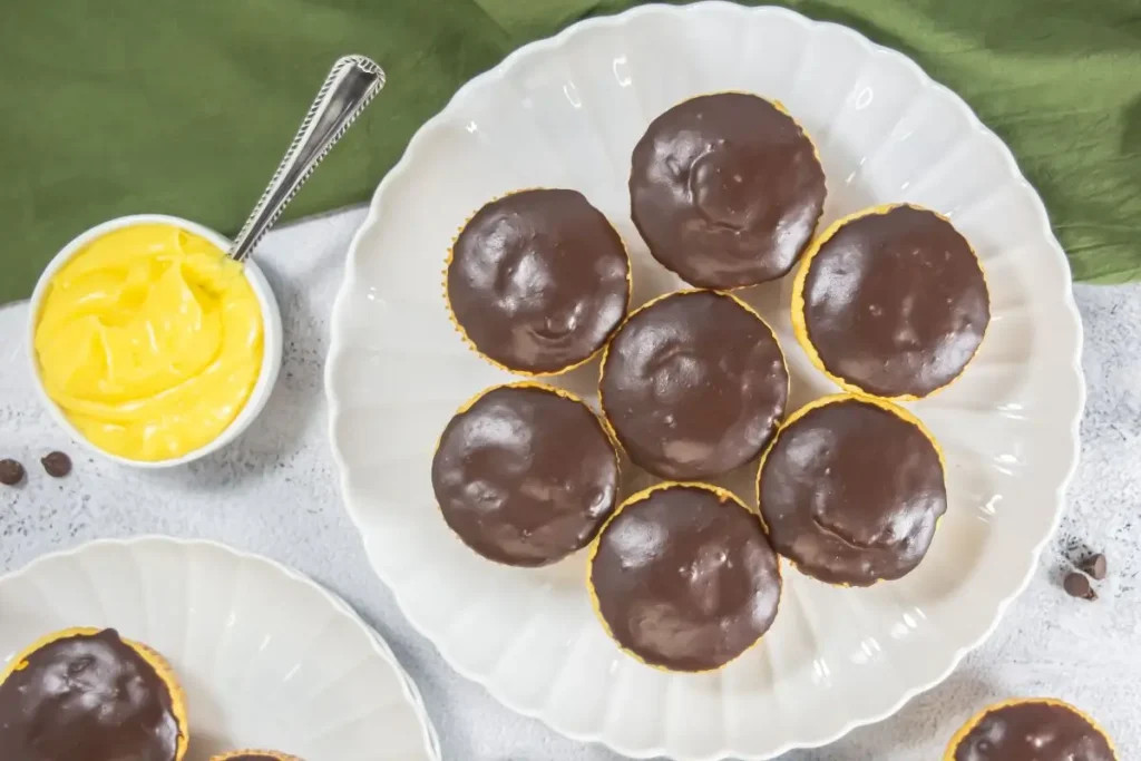 Boston Cream Pie Cupcakes Seven ganache-topped cupcakes on a white platter beside a bowl of yellow pudding