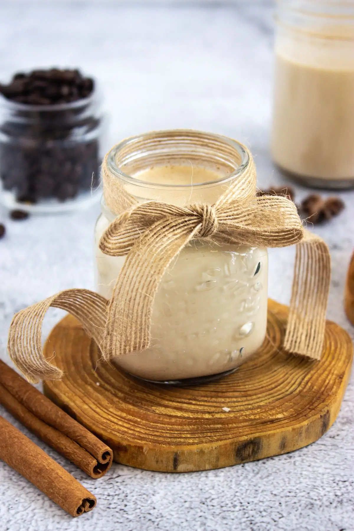 Homemade Cinnamon Vanilla Creamer (Cinnabon-Style) Mason jar of barista-style latte enhancer on a wooden coaster, surrounded by cinnamon sticks and coffee beans
