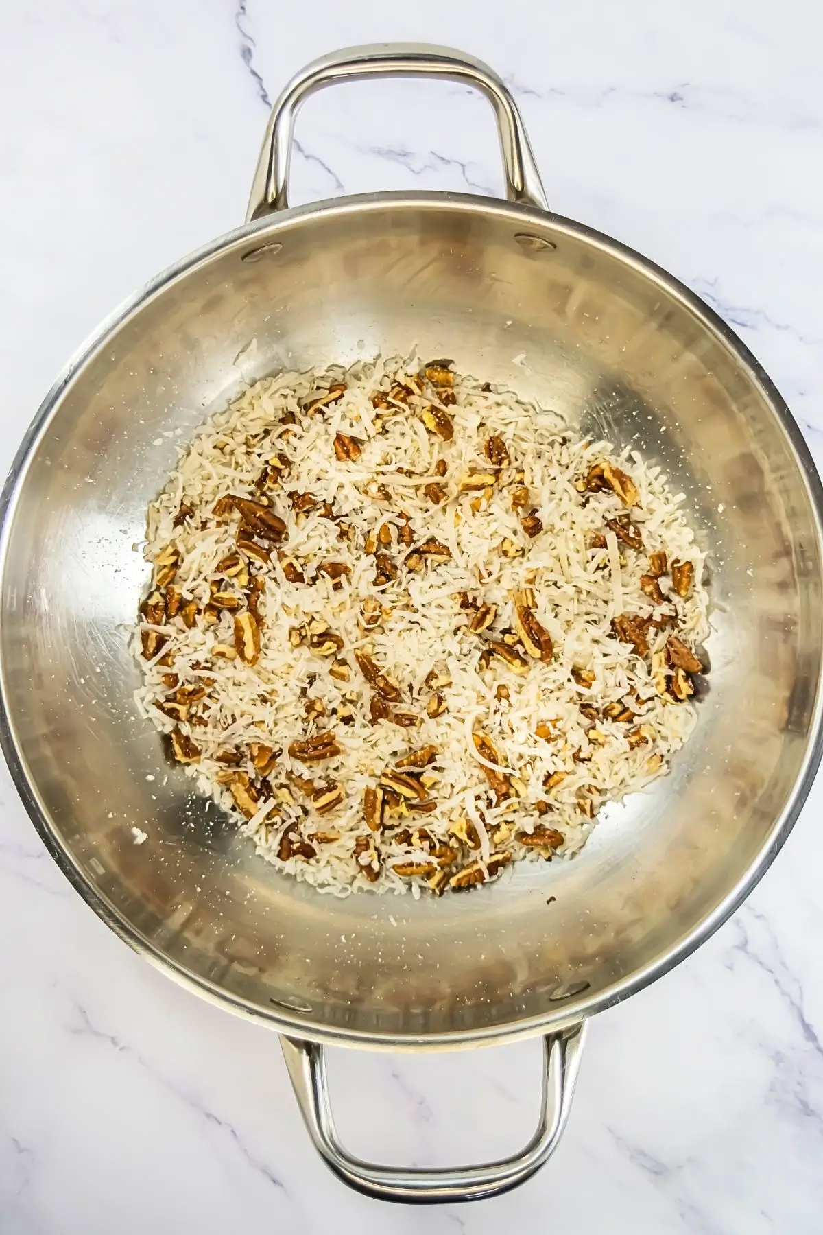 German Chocolate Cake Crumbl Cookies German chocolate frosting being made in a saucepan with toasted coconut and chopped pecans for Crumbl cookie copycat recipe.