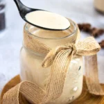 Black spoon scooping Cinnabon-inspired coffee creamer from a rustic mason jar