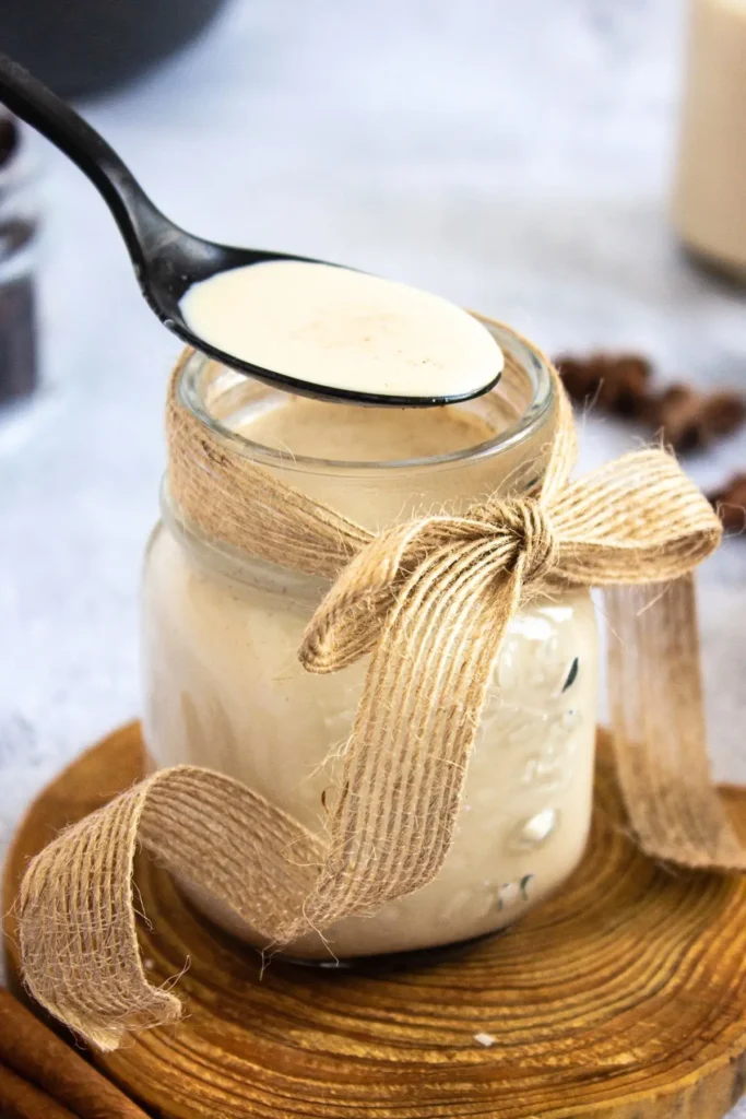 Black spoon scooping Cinnabon-inspired coffee creamer from a rustic mason jar