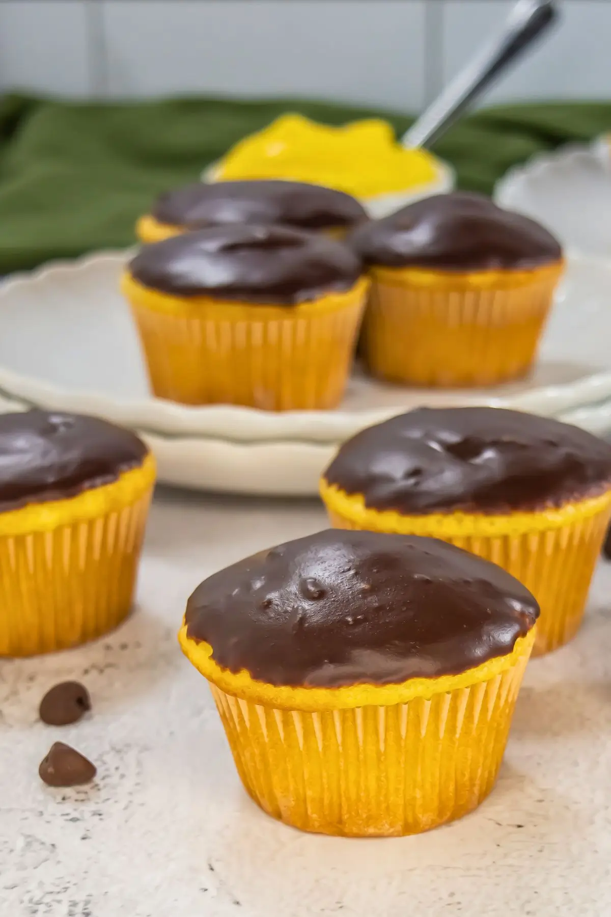 Boston Cream Pie Cupcakes Six vanilla cupcakes with chocolate ganache on a white surface